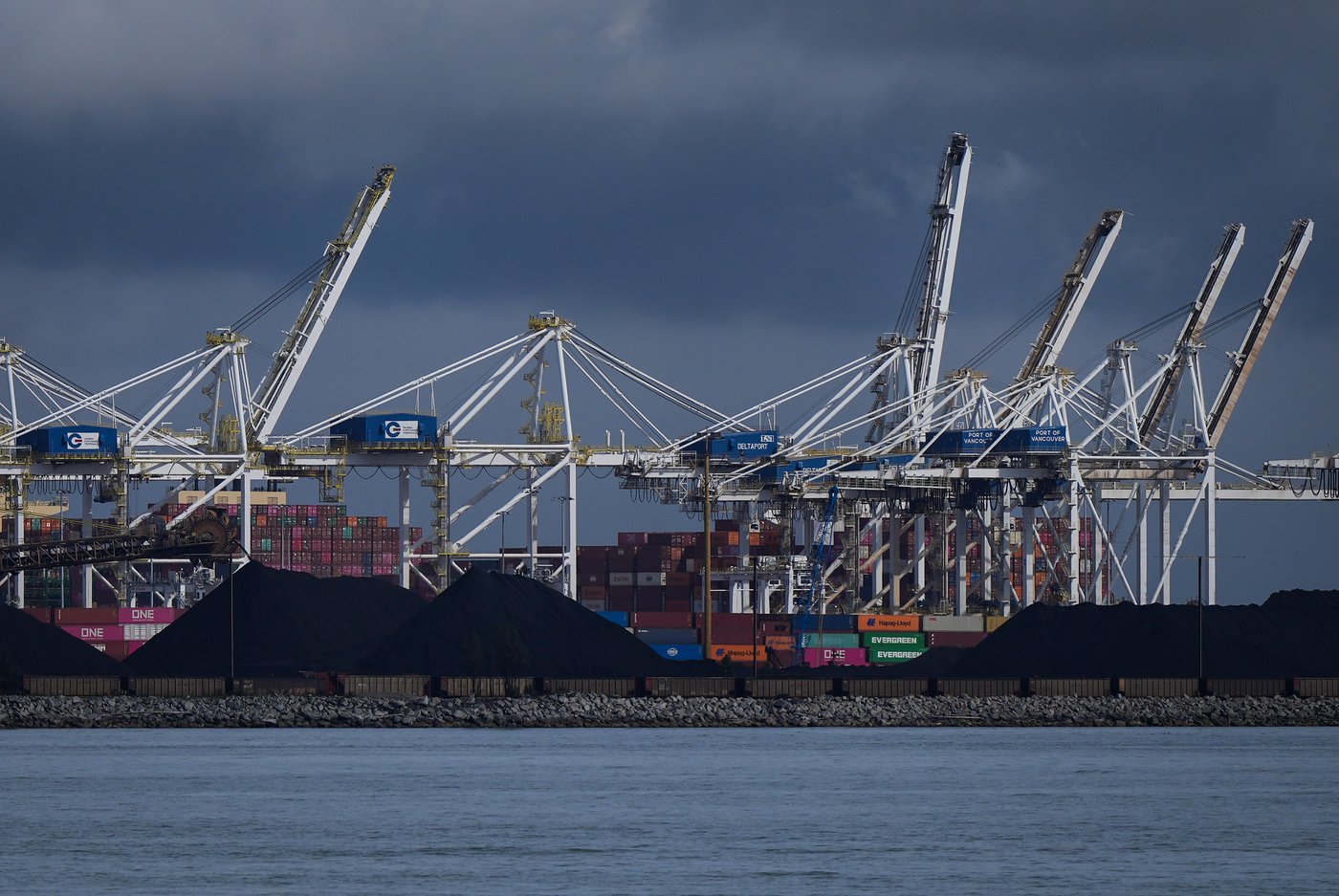 Piles of coal awaiting export and gantry cranes used to load and unload containers onto and from cargo ships are seen at Deltaport, in Delta, B.C., on Monday, September 9, 2024. THE CANADIAN PRESS/Darryl Dyck